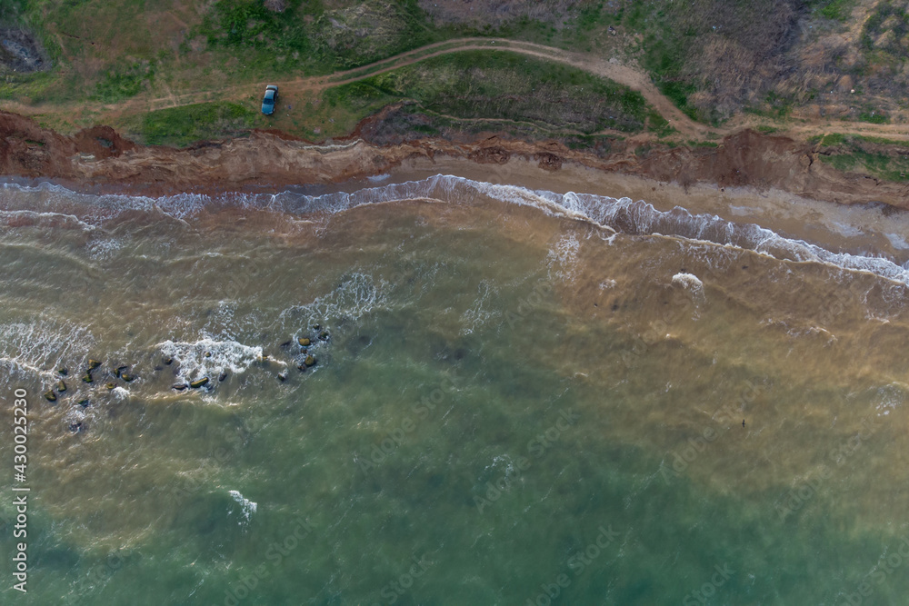 Steep sea shore and surf. Sea water muddy with sand after storm and algae. Aerial view.