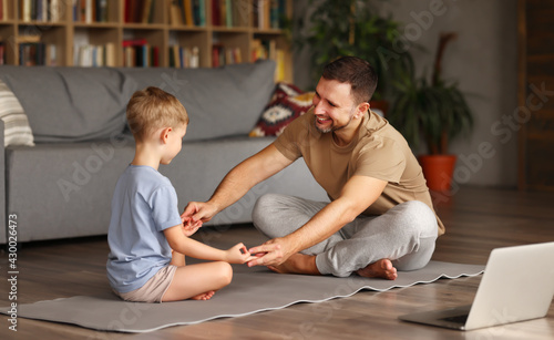 Young happy father teaching child meditation techniques while having online yoga class