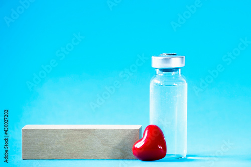 Safe vaccination concept. Glass vial with red heart on blue background. photo