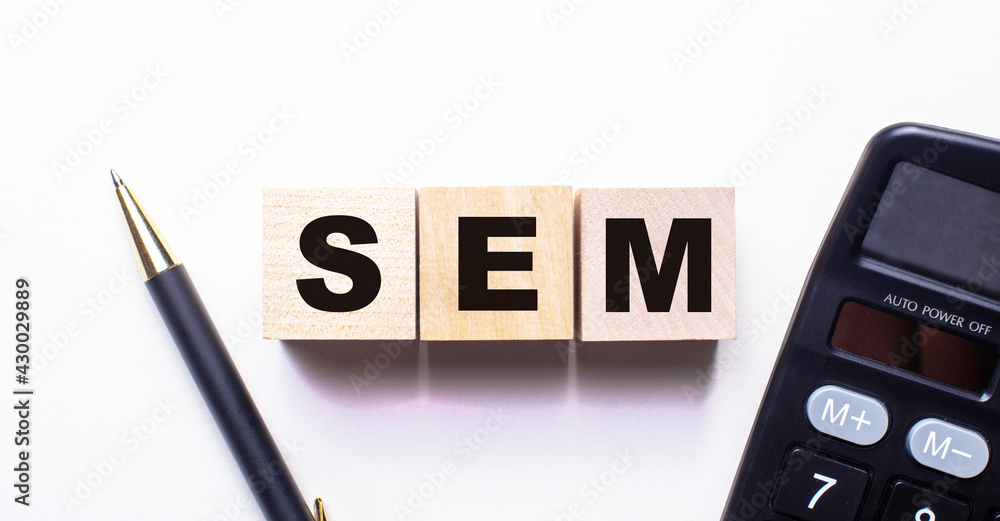 The word SEM is written on wooden cubes between a pen and a calculator on a light background. The word SEM is written on wooden cubes between a pen and a calculator on a light background.