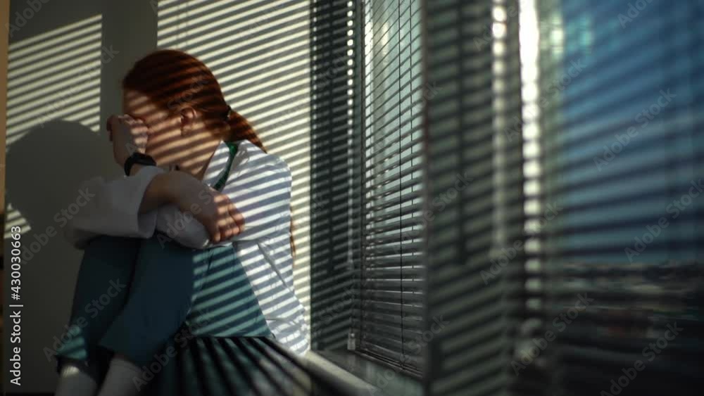 Tracking shot of unhappy frustrated female doctor crying sitting near window in sunny day. Stressed upset young woman physician feeling worried about professional malpractice. Shooting in slow motion. Tracking shot of unhappy frustrated female doctor crying sitting near window in sunny day. Stressed upset young woman physician feeling worried about professional malpractice. Shooting in slow motion.