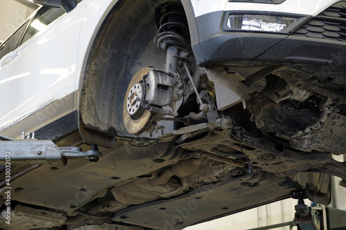 Modern car in a car service on a lift. The wheel is removed from the car. Elements of the car's suspension, parts of the brake system are visible.