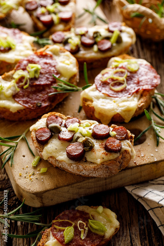 Grilled bruschetta with cheese, sausage and herbs on a wooden board, close-up view. Party food idea
