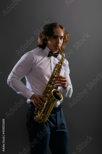 Studio portrait of young cool man with saxophone on dark background.