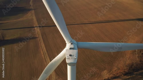 Close up a large spinning wind turbine on the background of wind farm at sunset. 