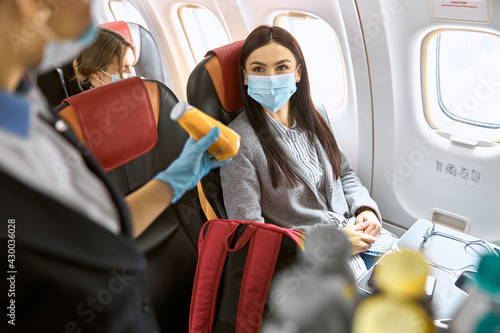 New order in airplane. Woman is sitting in mask while stuardess proposes her drinks