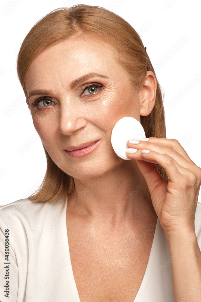 Portrait of a beautiful elderly woman in a white shirt removing makeup with a cleanser and a cotton pad. Portrait of a beautiful elderly woman in a white shirt removing makeup with a cleanser and a cotton pad.