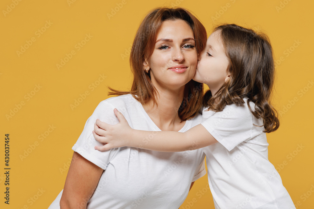 Happy woman in white t-shirt have fun with cute child baby girl 5-6 years old kiss cheek. Mommy little kid daughter isolated on yellow orange color background studio. Mother's Day love family concept. Happy woman in white t-shirt have fun with cute child baby girl 5-6 years old kiss cheek. Mommy little kid daughter isolated on yellow orange color background studio. Mother's Day love family concept.