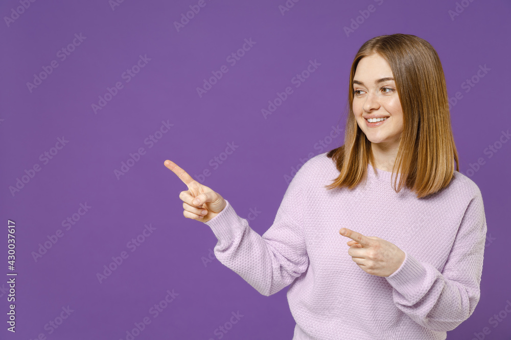 Young smiling happy cheerful friendly student caucasian woman 20s wear purple knitted sweater point index finger aside on copy space area mock up isolated on violet color background studio portrait Young smiling happy cheerful friendly student caucasian woman 20s wear purple knitted sweater point index finger aside on copy space area mock up isolated on violet color background studio portrait