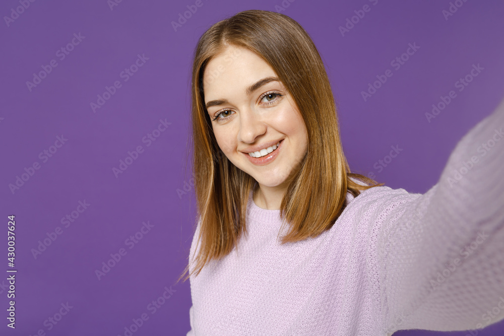 Close up young smiling happy student caucasian woman 20s wearing purple knitted sweater doing selfie shot on mobile phone isolated on violet color background studio portrait. People lifestyle concept. Close up young smiling happy student caucasian woman 20s wearing purple knitted sweater doing selfie shot on mobile phone isolated on violet color background studio portrait. People lifestyle concept.