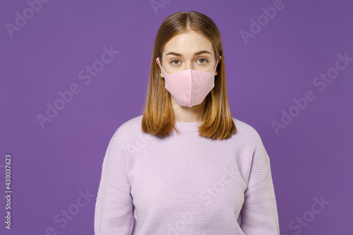 Young student caucasian woman 20s wear purple knitted sweater fabric face mask to safe from coronavirus virus covid-19 during pandemic quarantine isolated on violet color background studio portrait.