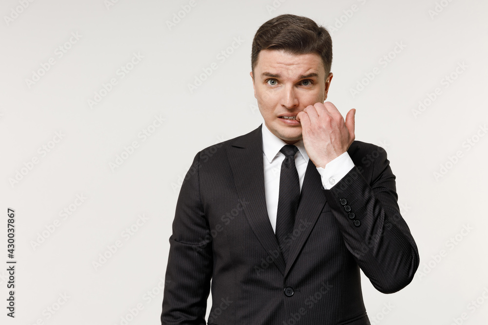 Close up young puzzled confused employee business corporate lawyer man 20s in classic formal black grey suit shirt tie work in office biting nails fingers isolated on white background studio portrait Close up young puzzled confused employee business corporate lawyer man 20s in classic formal black grey suit shirt tie work in office biting nails fingers isolated on white background studio portrait