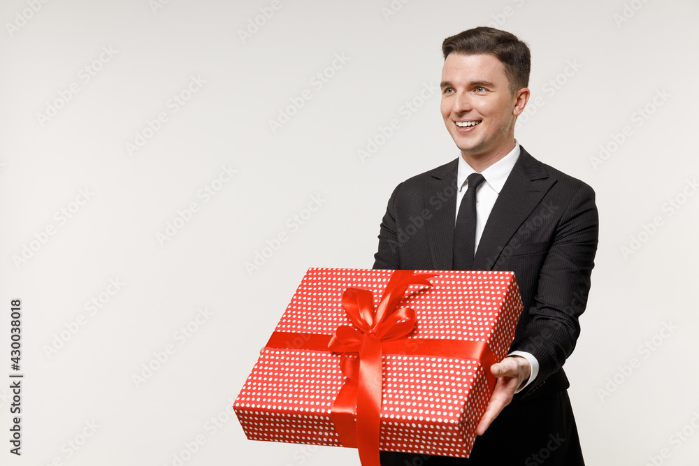 Young smiling employee business corporate lawyer man 20s wear classic black grey suit shirt tie work in office hold red present box with gift ribbon bow isolated on white background studio portrait Young smiling employee business corporate lawyer man 20s wear classic black grey suit shirt tie work in office hold red present box with gift ribbon bow isolated on white background studio portrait