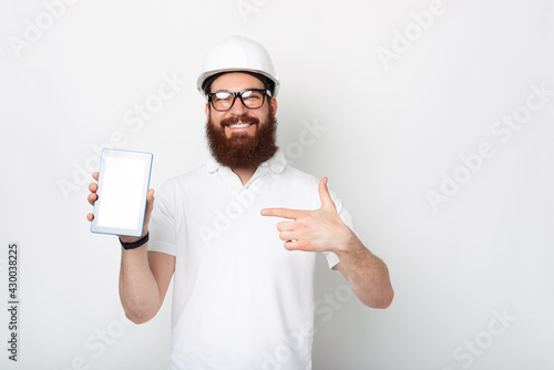 Young engineer dressed in white uniform is pointing at his tablet.