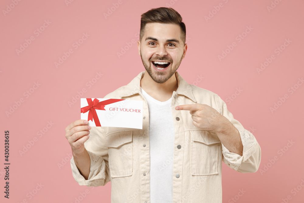 Young satisfied fun happy rich man 20s wearing jacket white t-shirt point index finger on gift voucher flyer mock up isolated on pastel pink color background studio portrait. Lifestyle people concept Young satisfied fun happy rich man 20s wearing jacket white t-shirt point index finger on gift voucher flyer mock up isolated on pastel pink color background studio portrait. Lifestyle people concept