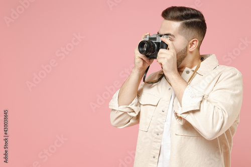 Young european tourist trendy man 20s wearing jacket white t-shirt holding retro vintage camera taking photo isolated on pastel pink color background studio portrait. Photography lifestyle concept
