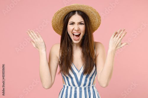 Young angry irritated stressed caucasian woman 20s wear summer clothes striped dress straw hat spread hands scream shout isolated on pastel pink background studio portrait. People lifestyle concept. © ViDi Studio