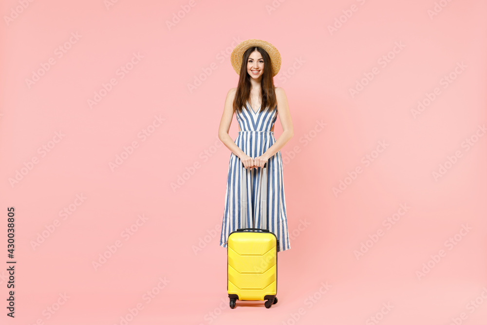 Full length traveler tourist woman 20s in summer clothes, hat hold yellow valise suitcase isolated on pastel pink background. Passenger traveling abroad on weekends getaway Air flight journey concept