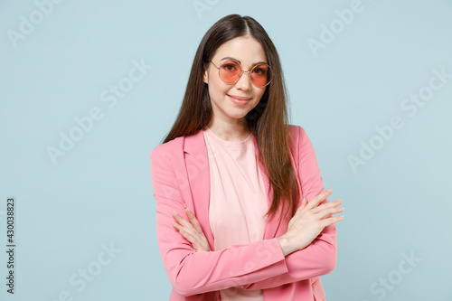 Young fun smiling happy confident caucasian trendy fashionable woman 20s in pastel pink clothes glasses hold hands crossed folded isolated on blue background studio portrait. People lifestyle concept.