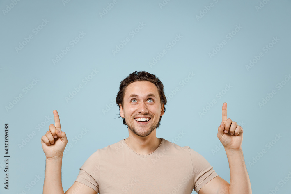 Young smiling happy positive friendly man 20s wearing casual basic beige t-shirt point index finger overhead on workspace area mock up copy space isolated on pastel blue background studio portrait Young smiling happy positive friendly man 20s wearing casual basic beige t-shirt point index finger overhead on workspace area mock up copy space isolated on pastel blue background studio portrait