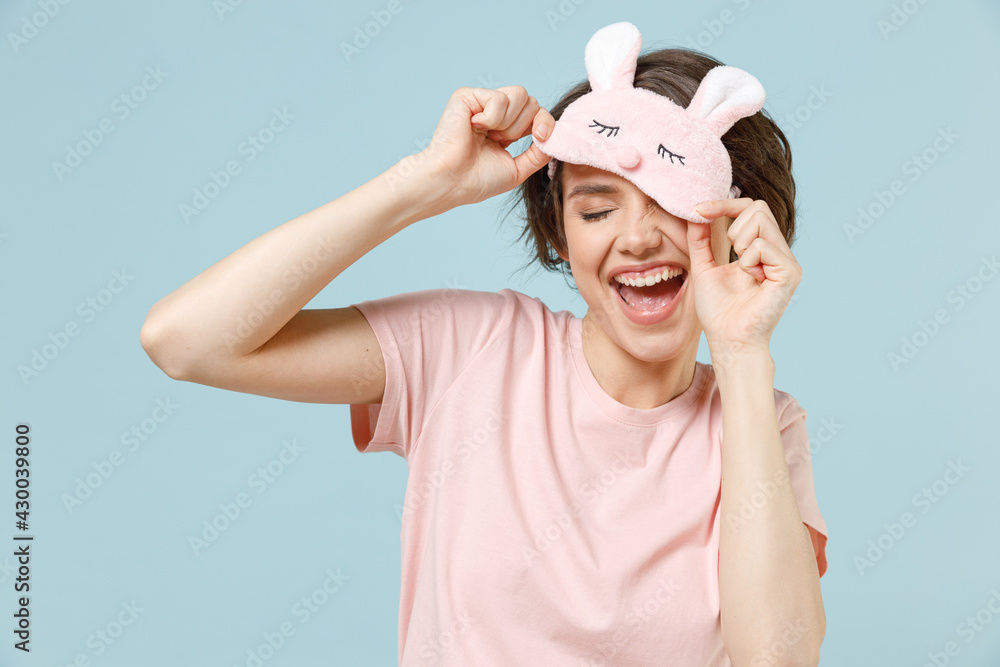 Young fun happy caucasian woman 20s wear pajamas jam sleep rest relaxing at home took off blindfold eye mask isolated on pastel blue color background studio portrait. Good mood night bedtime concept. Young fun happy caucasian woman 20s wear pajamas jam sleep rest relaxing at home took off blindfold eye mask isolated on pastel blue color background studio portrait. Good mood night bedtime concept.