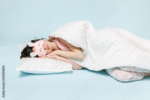 Full length young sleeping calm woman in pajamas jam sleep eye mask rest relax at home lying lie wrap cover blanket duvet on pillow isolated on pastel blue background. Good mood night bedtime concept
