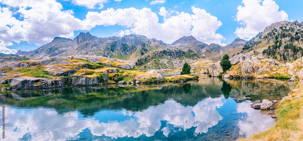 Panoramic view of mountainous landscape reflected in a lake with a beautiful mountains on a sunny summer day. Concept of mountain trip. Circo Saboredo, Aran Valley, Pyrenees, Catalonia, Spain.