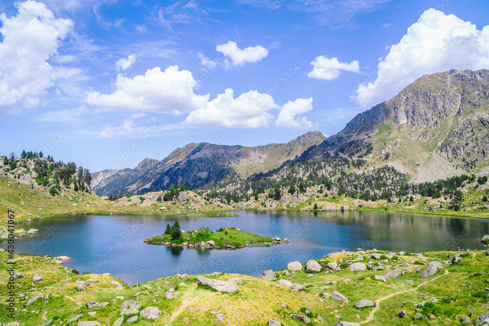 Beautiful Mountain lake surrounded by mountains with green grass on a lovely sunny summer day. Concept of mountain trip and summer vacations. Circo Saboredo, Aran Valley-Pyrenees, Catalonia, Spain.