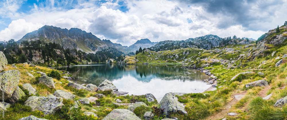Panoramic view of mountain lake surrounded by mountains reflected in the water. Concept of mountain trip, summer vacations and nature. Circo Saboredo, Aran Valley-Pyrenees, Catalonia, Spain.