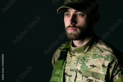 Thoughtful young military soldier in camouflage clothing looking away over dark background © Ivan