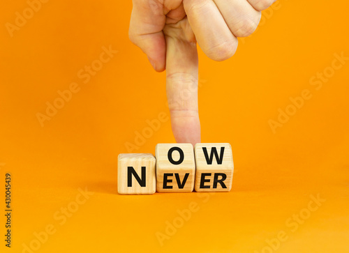 Now or never symbol. Businessman turns wooden cubes and changes the word 'never' to 'now' or vice versa. Beautiful orange background, copy space. Business and now or never concept.