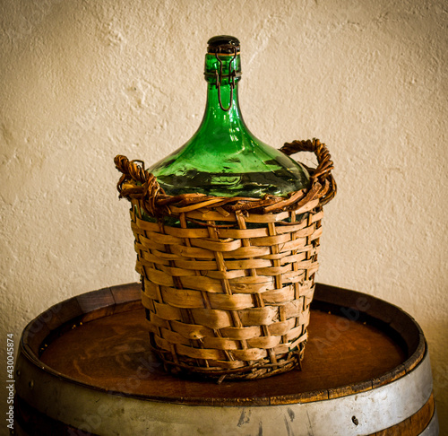 Canvas Print Ancient green glass carboy with wicker weave on a white wall background