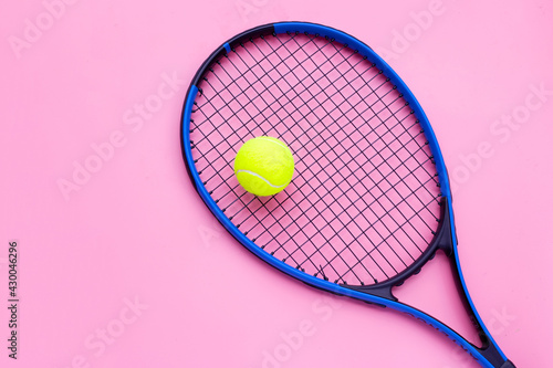 Tennis racket with ball on pink background.