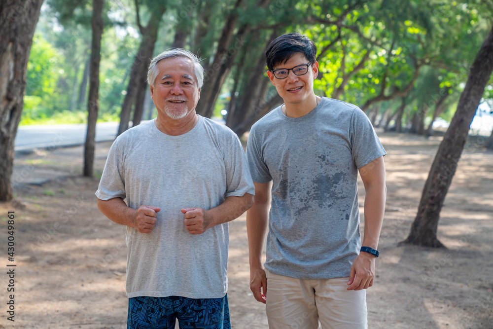 Happy Asian senior father and adult son do sport exercising on the beach together in summer morning. Healthy man with retirement elderly father relax and enjoy outdoor lifestyle activity on vacation