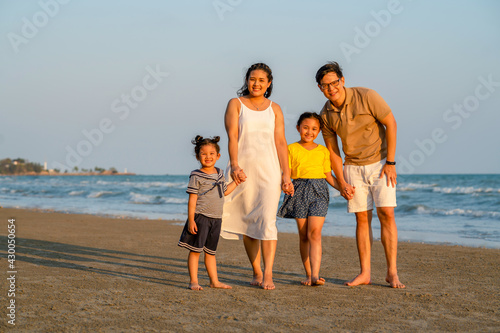 Portrait of Happy family on summer holiday vacation. Asian couple with two child girl kid holding hands and walking together on tropical beach. Family enjoy and having fun outdoor lifestyle in summer.