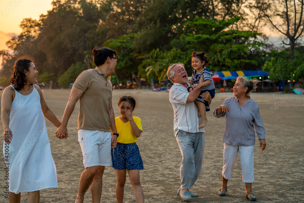 Fototapeta premium Happy big Asian family on beach holiday vacation. Multi-generation family holding hands and walking together on tropical beach at summer sunset. Family enjoy and having fun outdoor activity lifestyle.