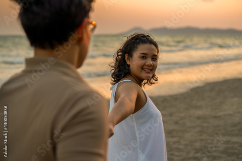 Happy Asian family on beach travel vacation. Adult couple holding hand and walking together on the beach at summer sunset. Smiling husband and wife relax and enjoy romantic outdoor lifestyle activity