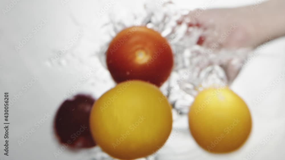 Person throws small ripe red and yellow cherry tomatoes into clear water on white background extreme close bottom view slow motion Person throws small ripe red and yellow cherry tomatoes into clear water on white background extreme close bottom view slow motion