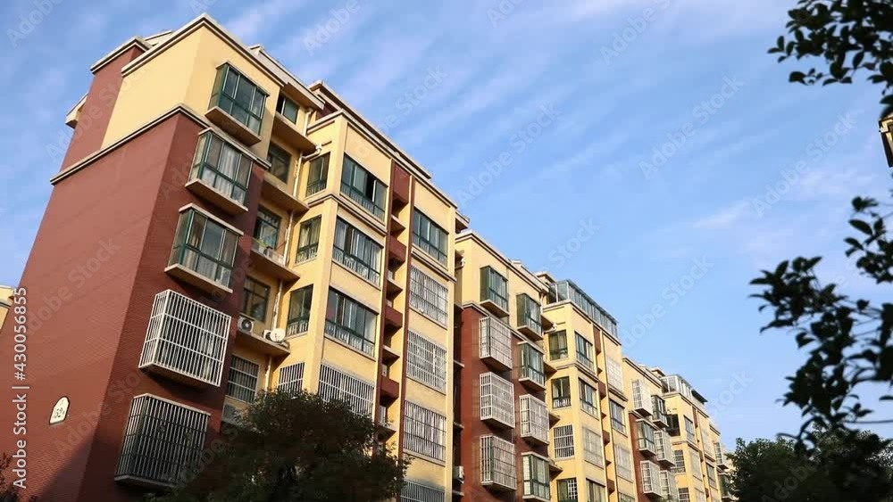 Low-angle shot of a residential building in China under blue sky with trees in foreground Low-angle shot of a residential building in China under blue sky with trees in foreground