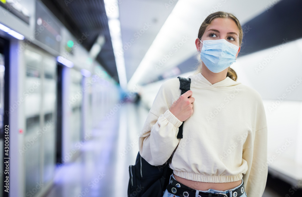 Young woman in face mask waiting for train on platform of subway underground station