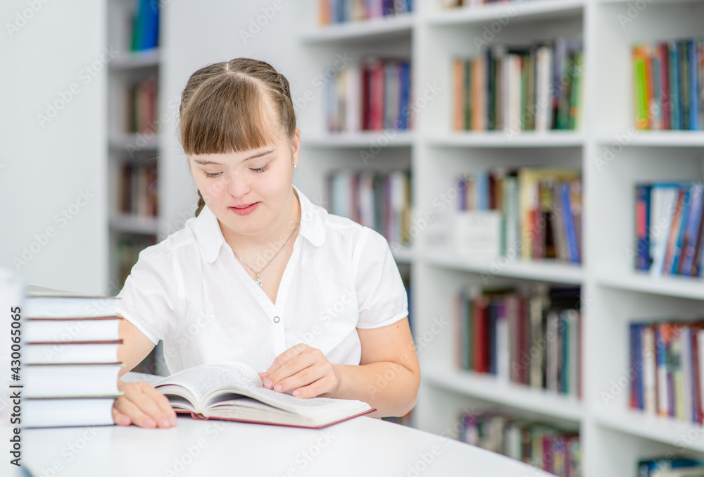 Girl with syndrome down reads a book at library. Education for disabled children concept Girl with syndrome down reads a book at library. Education for disabled children concept