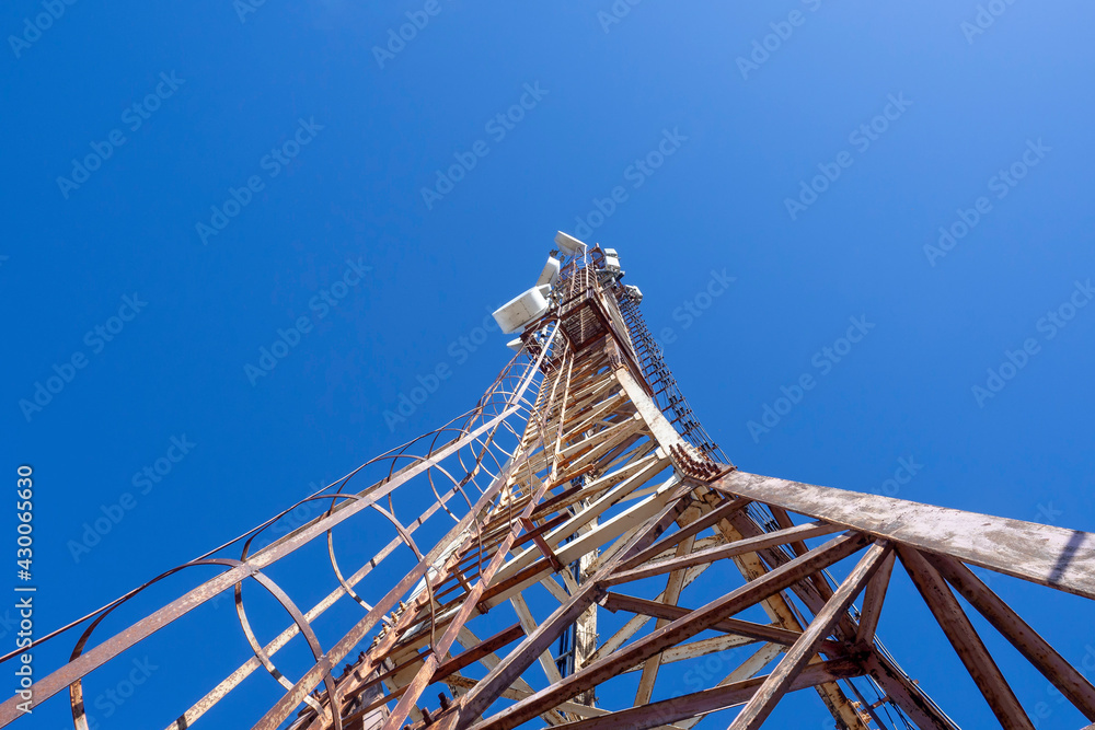 Mobile communications repeater tower, digital television. Metal tower against the blue sky, bottom view.