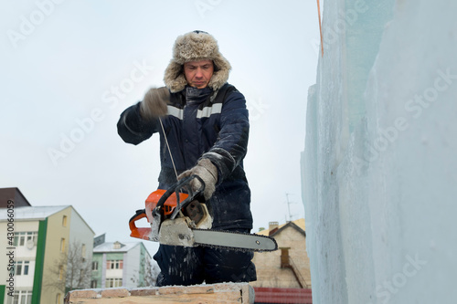 Worker assembler in blue jacket and fur hat on scaffolding with chainsaw