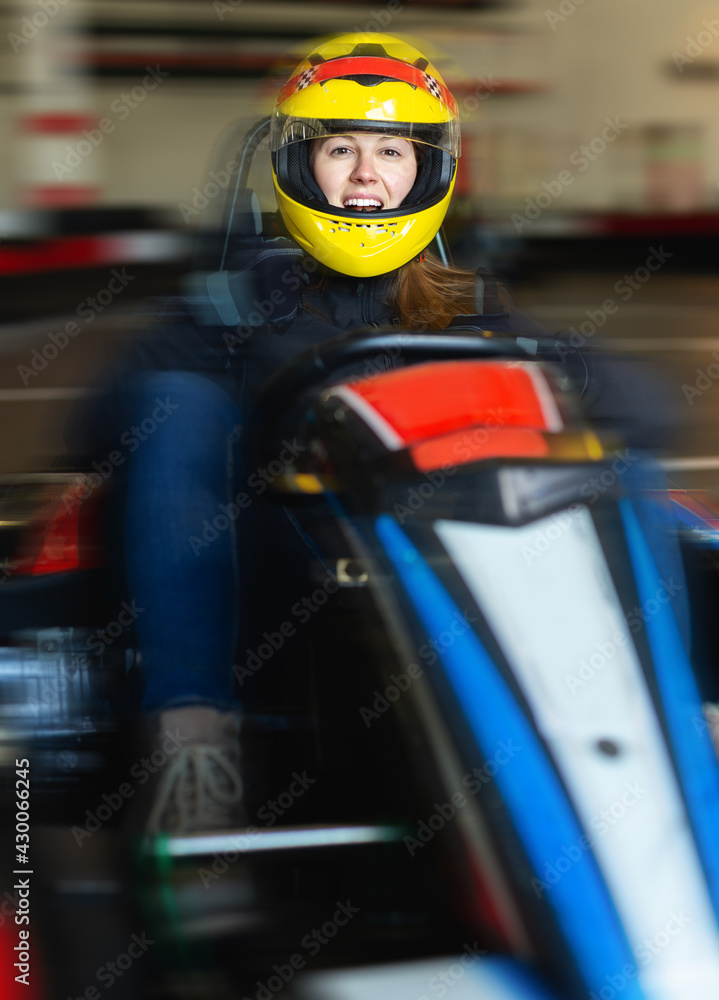 Positive woman with helmet sitting in car for karting in sport club