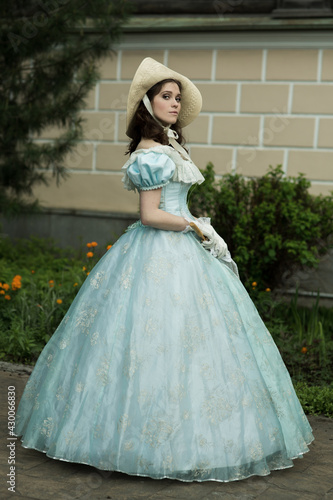 Fototapeta A beautiful young woman in a historical blue dress with an umbrella, gloves and a hat