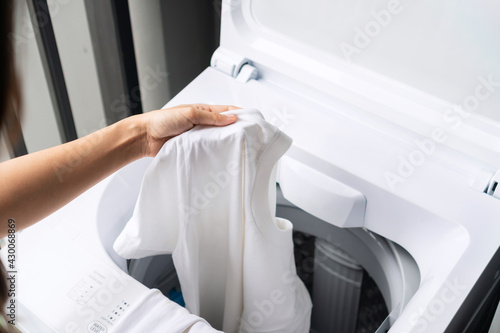Hnads of young woman putting white color clothes into washing machine at condominium. Laundry concept. Top view © Pattarisara