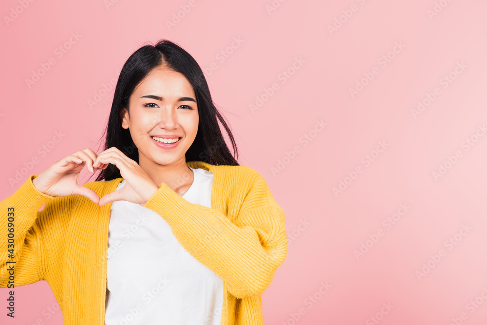 Happy Asian portrait beautiful cute young woman smile make finger heart gesture figure symbol shape sign with two hands sending love to her lover looking camera, studio shot isolated pink background Happy Asian portrait beautiful cute young woman smile make finger heart gesture figure symbol shape sign with two hands sending love to her lover looking camera, studio shot isolated pink background