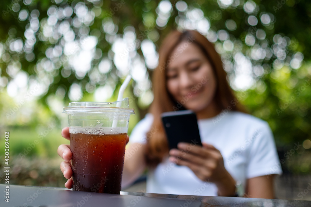 A young asian woman holding and using smart phone while drinking coffee in the outdoors A young asian woman holding and using smart phone while drinking coffee in the outdoors