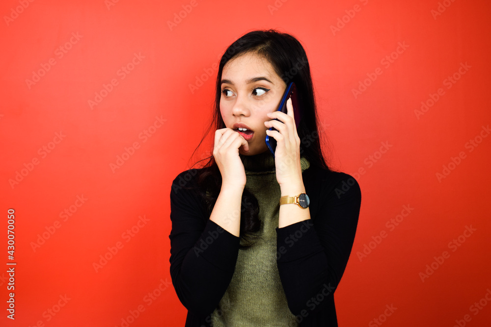 Portrait of Young beautiful asian women using black sweater talking on mobile phone with red isolated background Portrait of Young beautiful asian women using black sweater talking on mobile phone with red isolated background