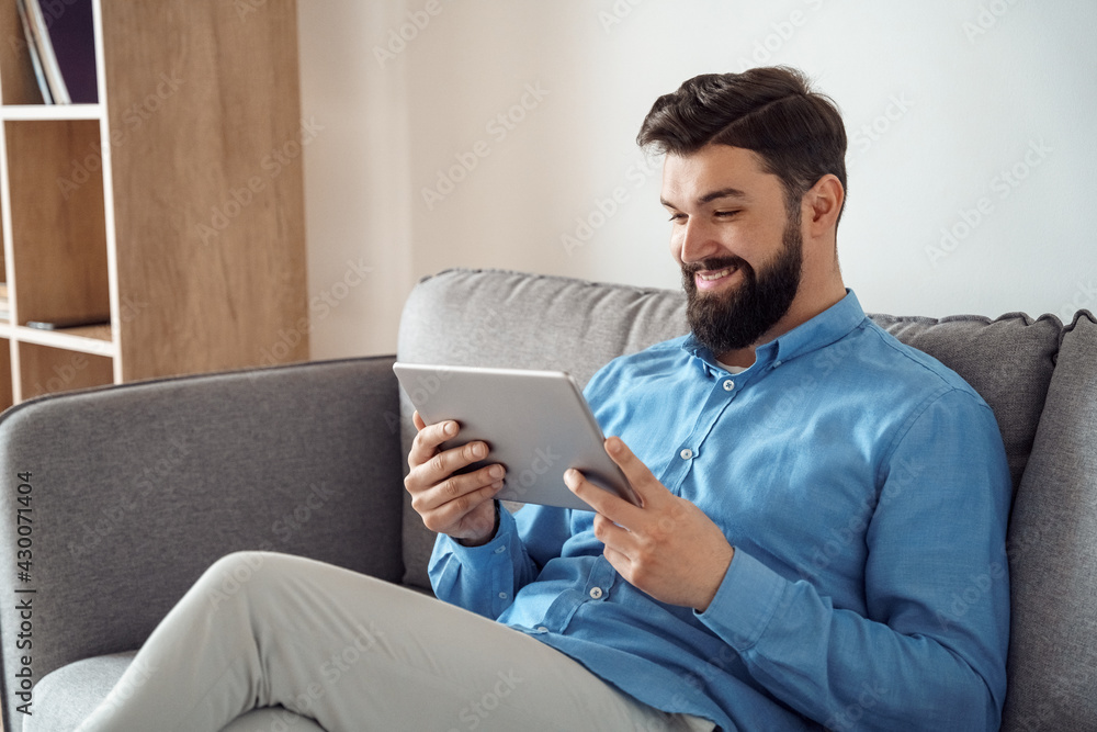 Smiling millennial caucasian man watching funny video using mobile tablet Smiling millennial caucasian man watching funny video using mobile tablet